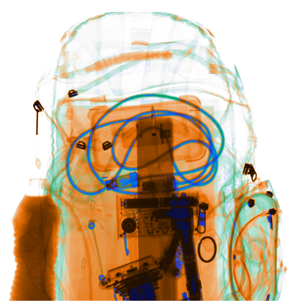 Security X-ray image of a backpack containing cables, electronic components, a bottle, and personal items.