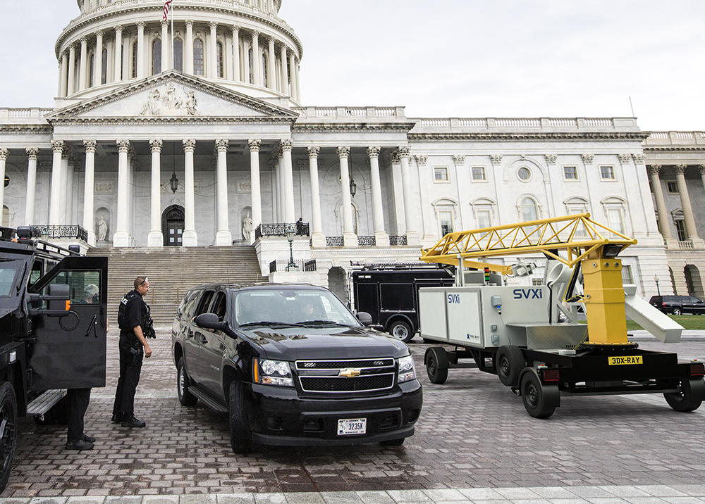 Black SUV parked in front of a building with a small yellow crane carrying an x-ray machine.